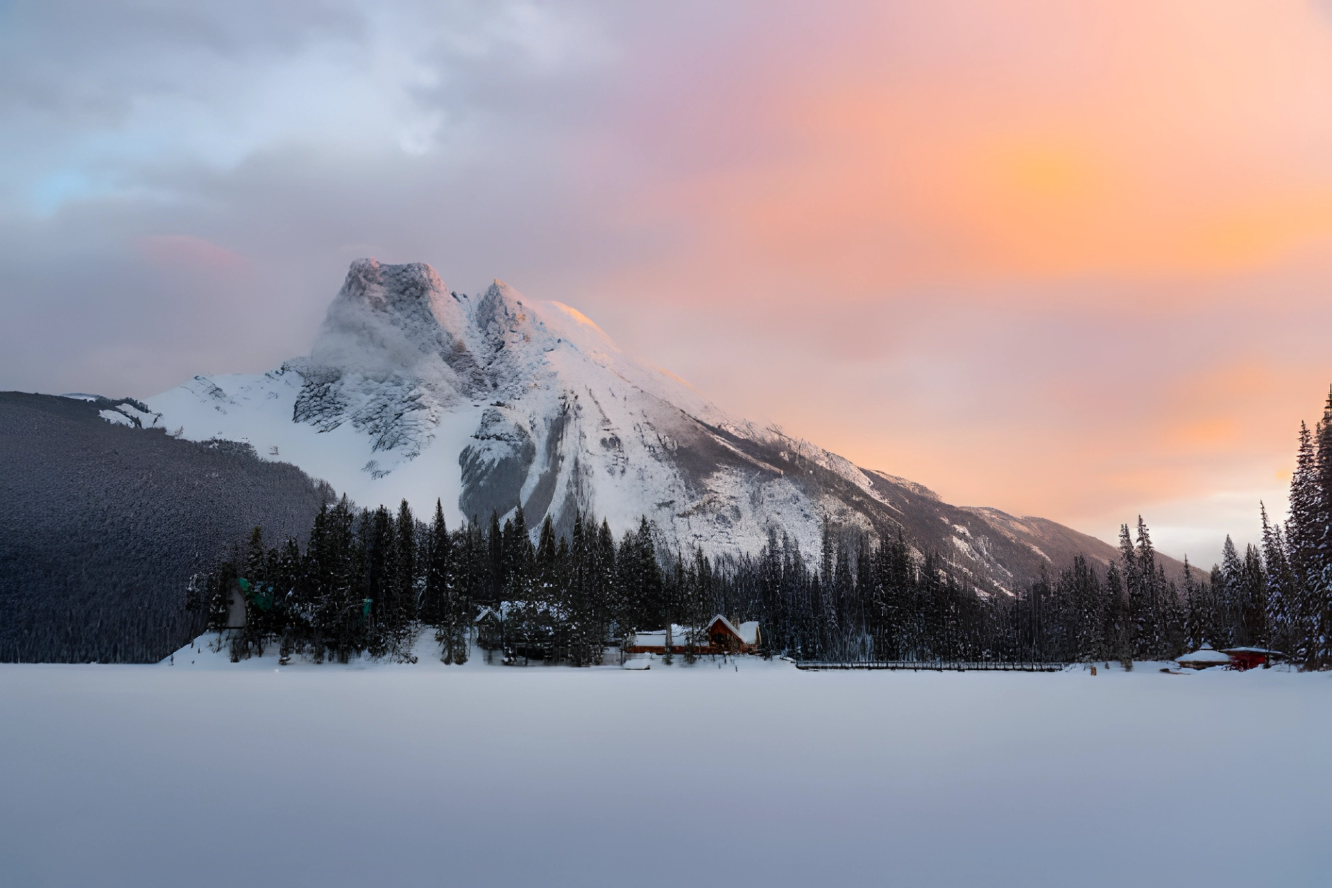 Snow-covered mountain at sunset with pine trees and cabins in Banff.