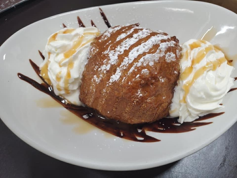 Fried ice cream with whipped cream, caramel drizzle, and chocolate syrup on white plate.