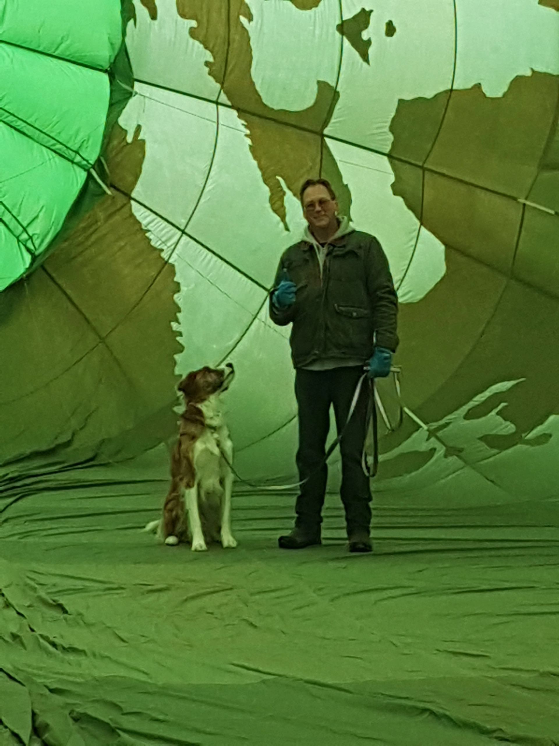 Person and dog inside inflated hot air balloon with globe-like pattern.