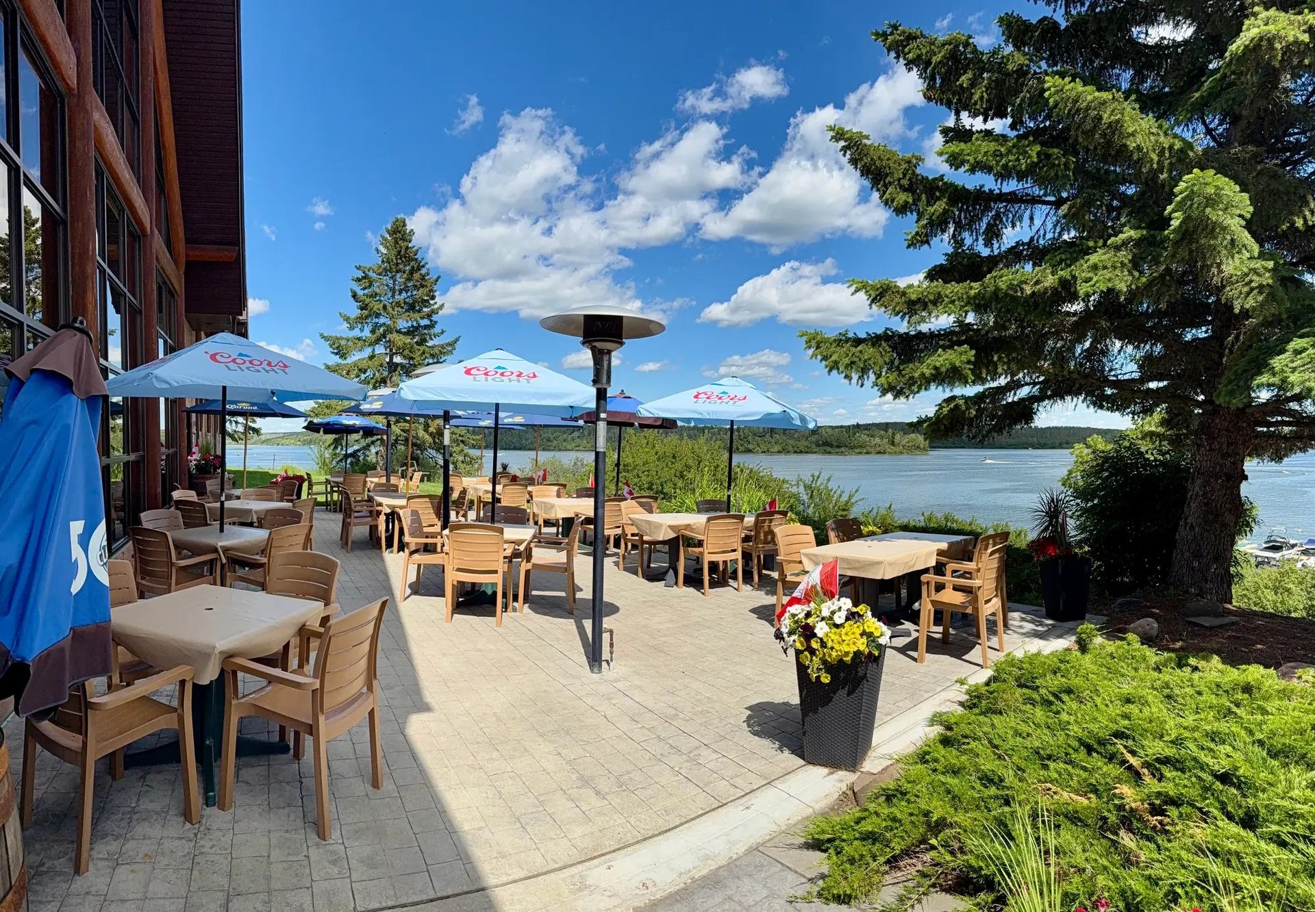 Restaurant patio with Coors Light umbrellas overlooking a lake, trees and blue sky.