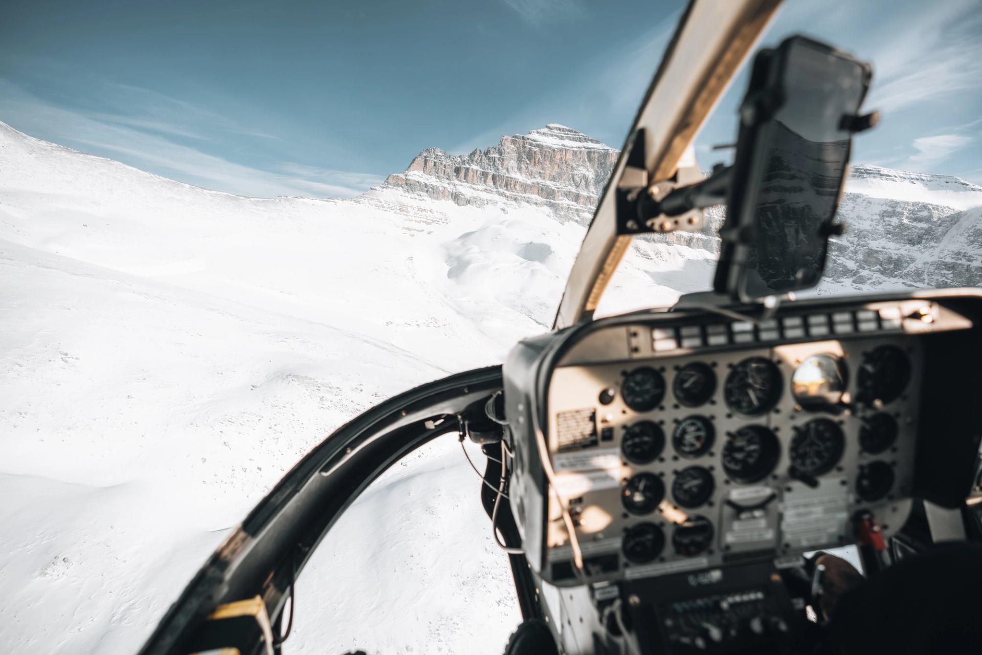 View from inside a helicopter flying over snowy mountain terrain.