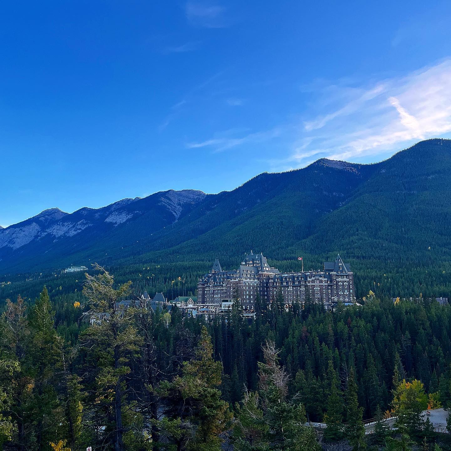 Fairmont Banff Springs hotel nestled in a forest with mountains under a blue sky.