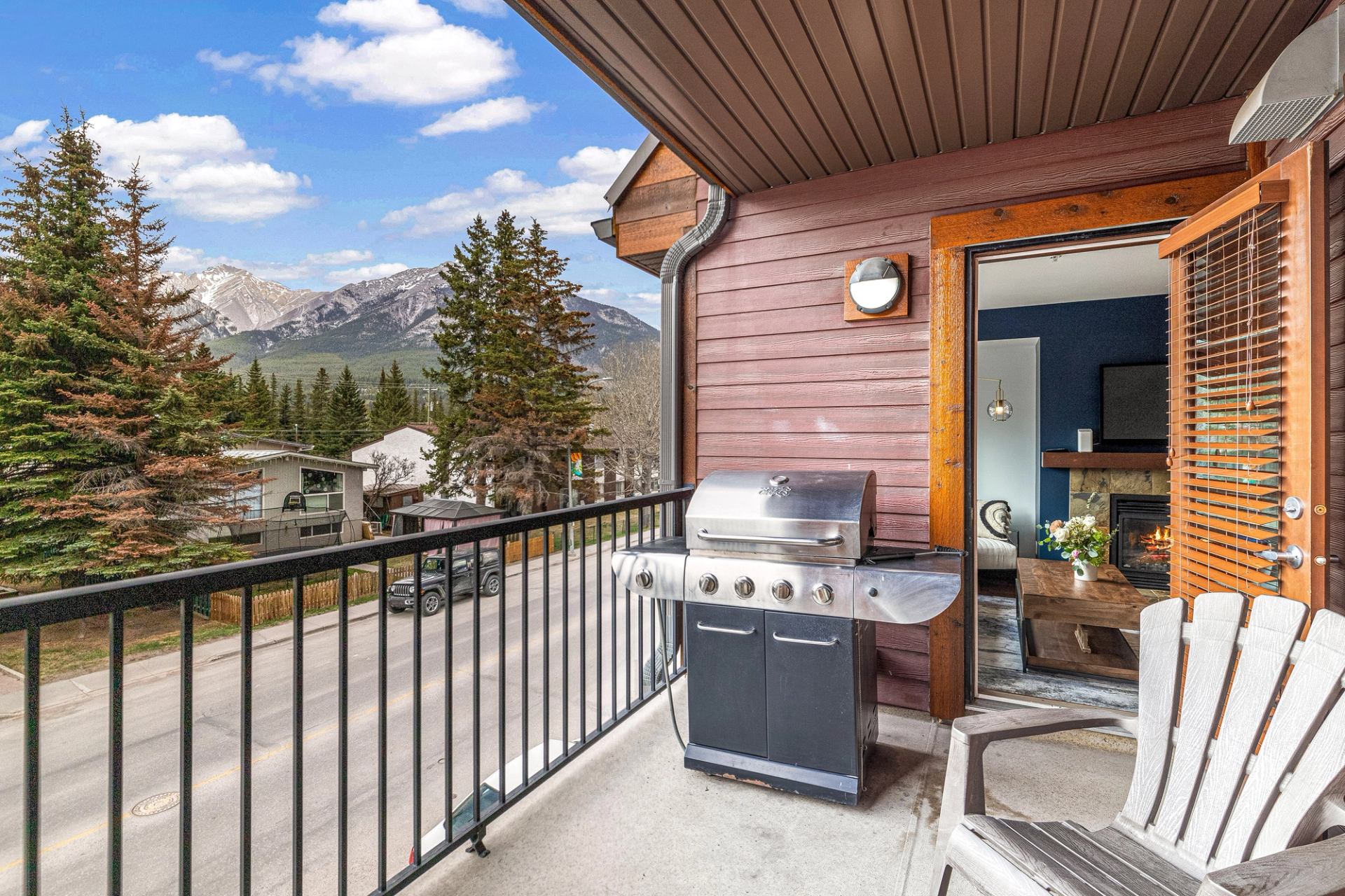Balcony with grill, seating, and mountain views near trees and rooftops.