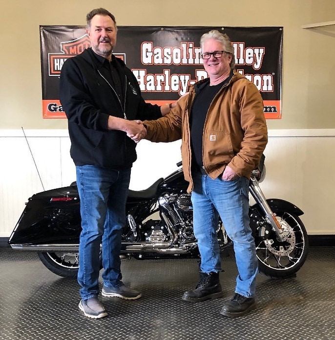 Two people shake hands in front of a black motorcycle at Gasoline Alley Harley-Davidson.