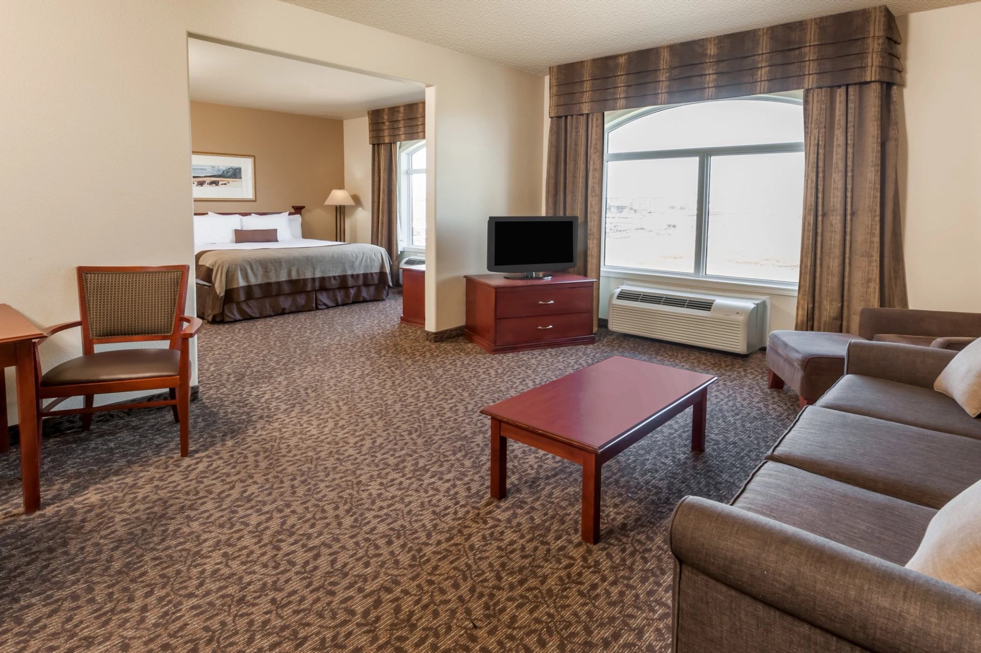 Hotel suite living area with sofa, coffee table, TV, and window curtains.