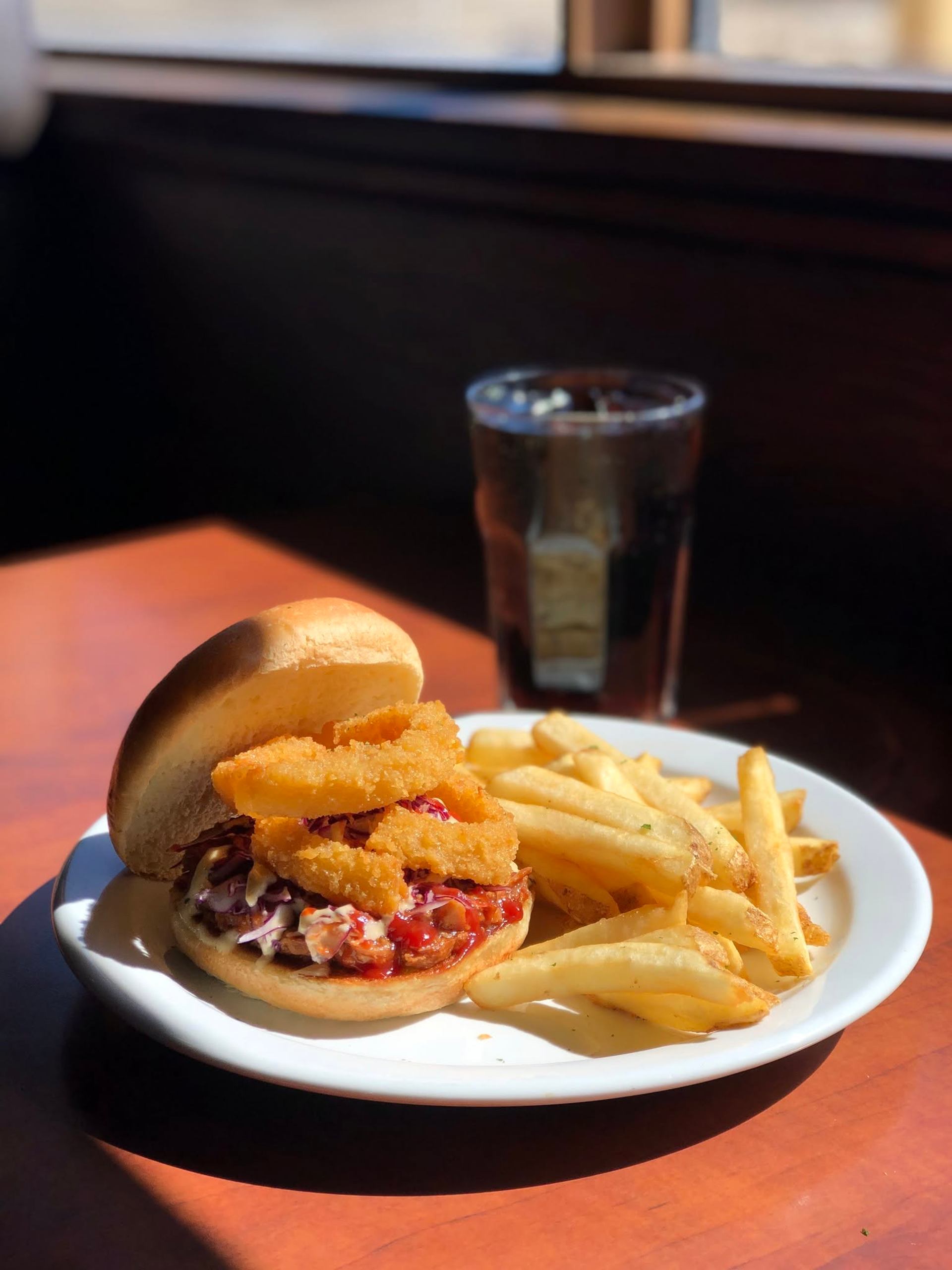 A burger topped with crispy onion rings is served with fries and a soft drink on a table.