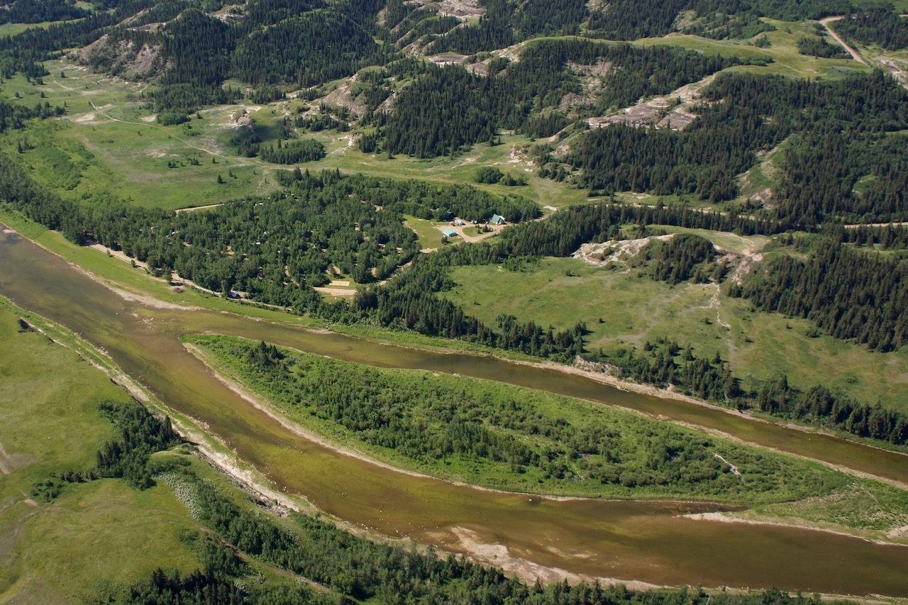 Aerial view of winding river through green fields and forested hills in Trenville Park.