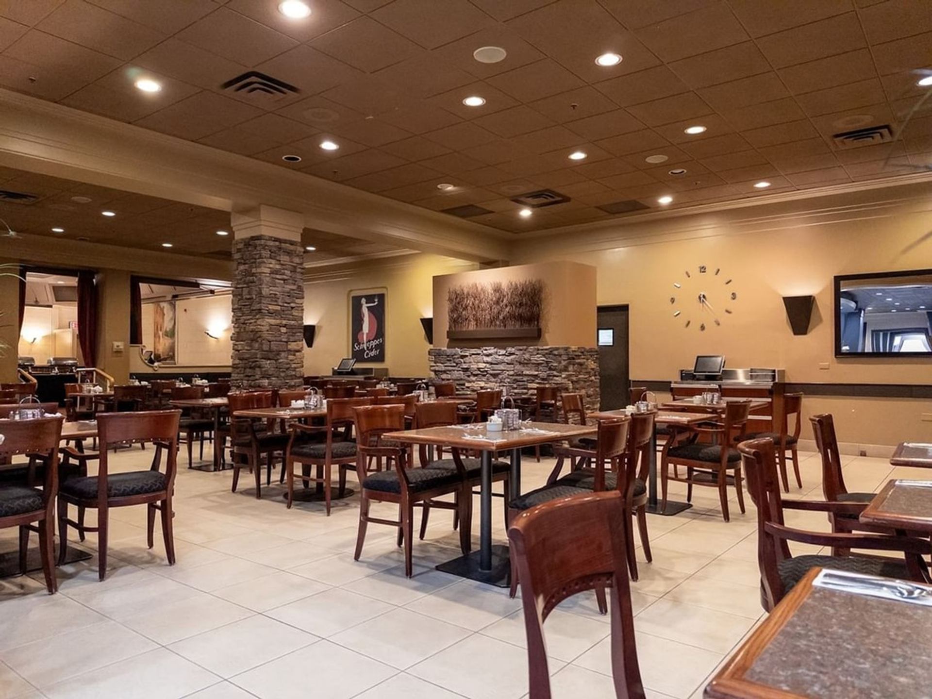 Restaurant dining room with wooden tables, chairs, stone accents and wall clock.