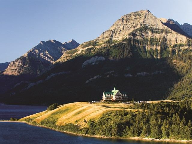 Waterton Valley shoreline with boat dock, grassy hills, and a castle-like building in mountains.