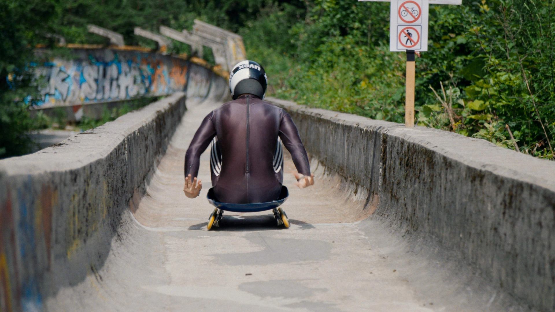Athlete riding a sled down an old concrete track surrounded by greenery.