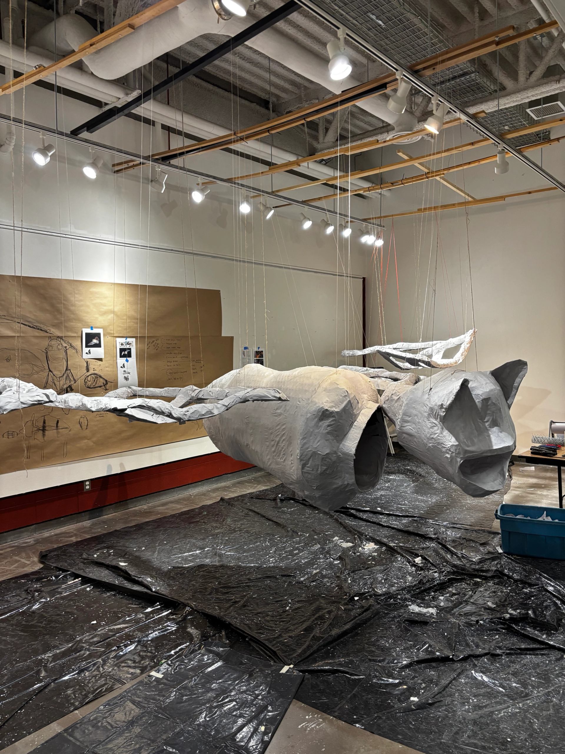 Suspended white sculptures in gallery with black floor covering and spotlighting.