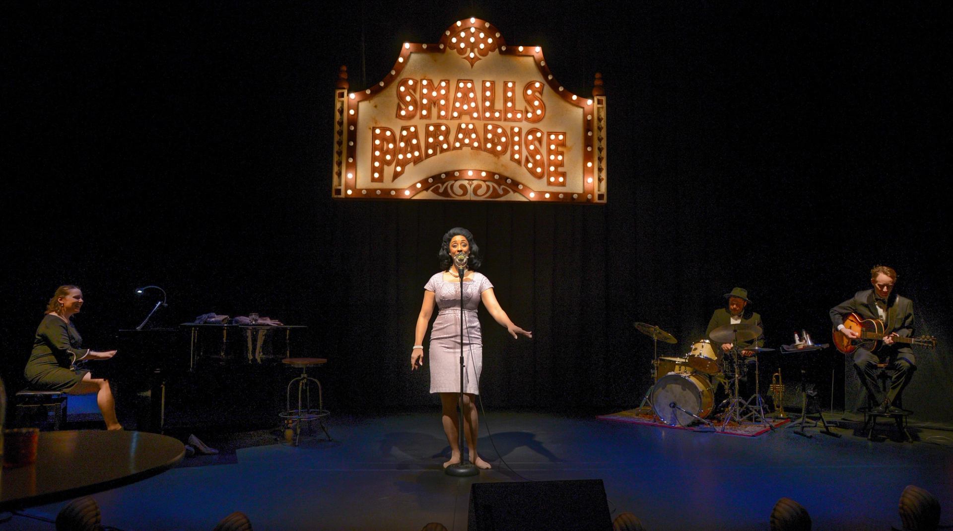 Singer performs on stage with pianist, drummer and guitarist under Smalls Paradise sign.