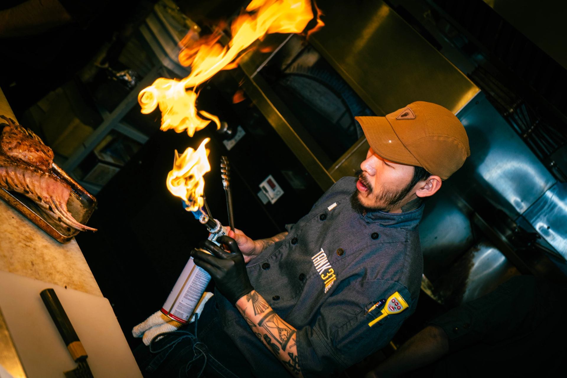 Chef using a blowtorch to flame-cook steak in the kitchen at The Grizzly Paw Brewing Company.