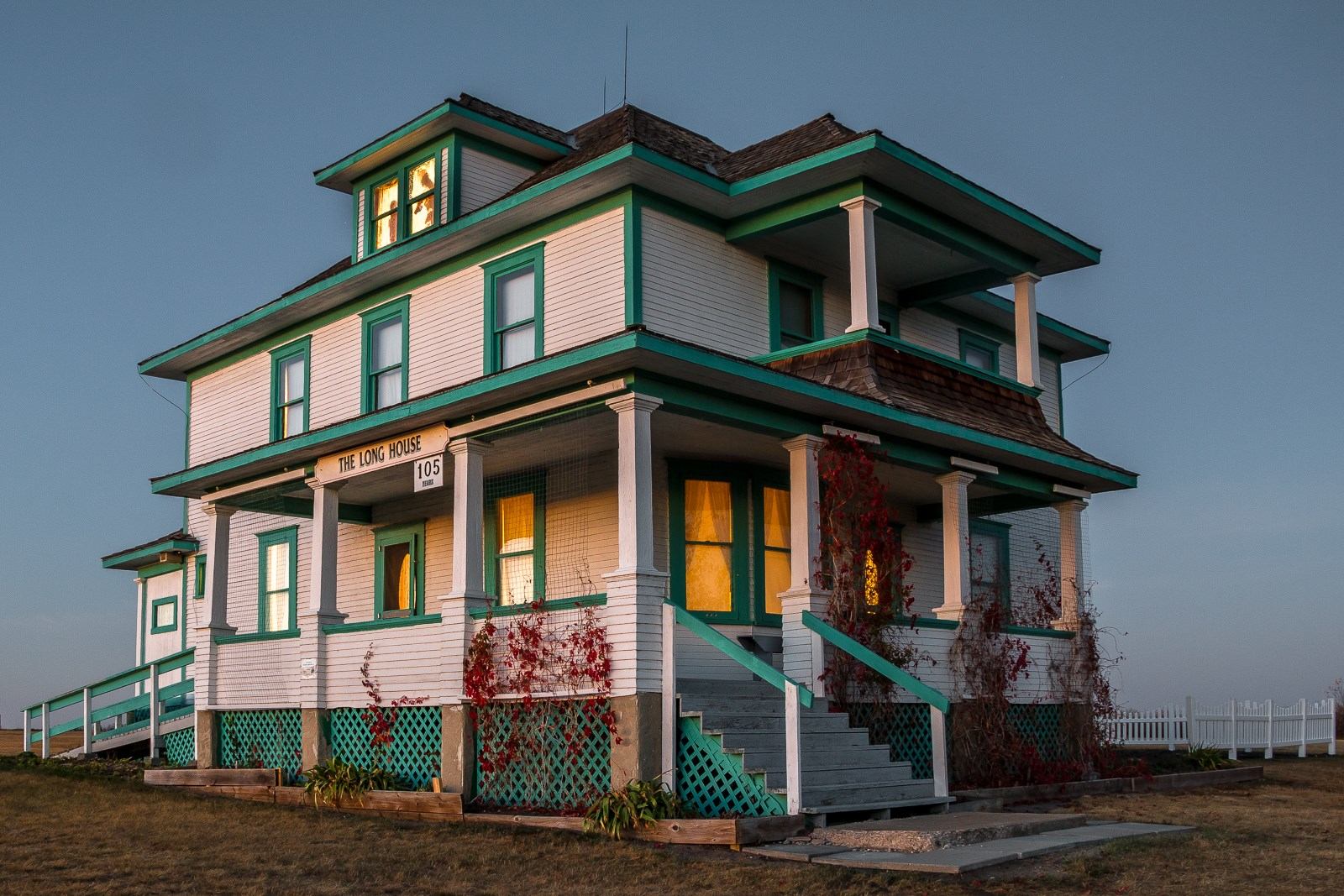 A photo of a three story white 1914 era ranch house with green trim.