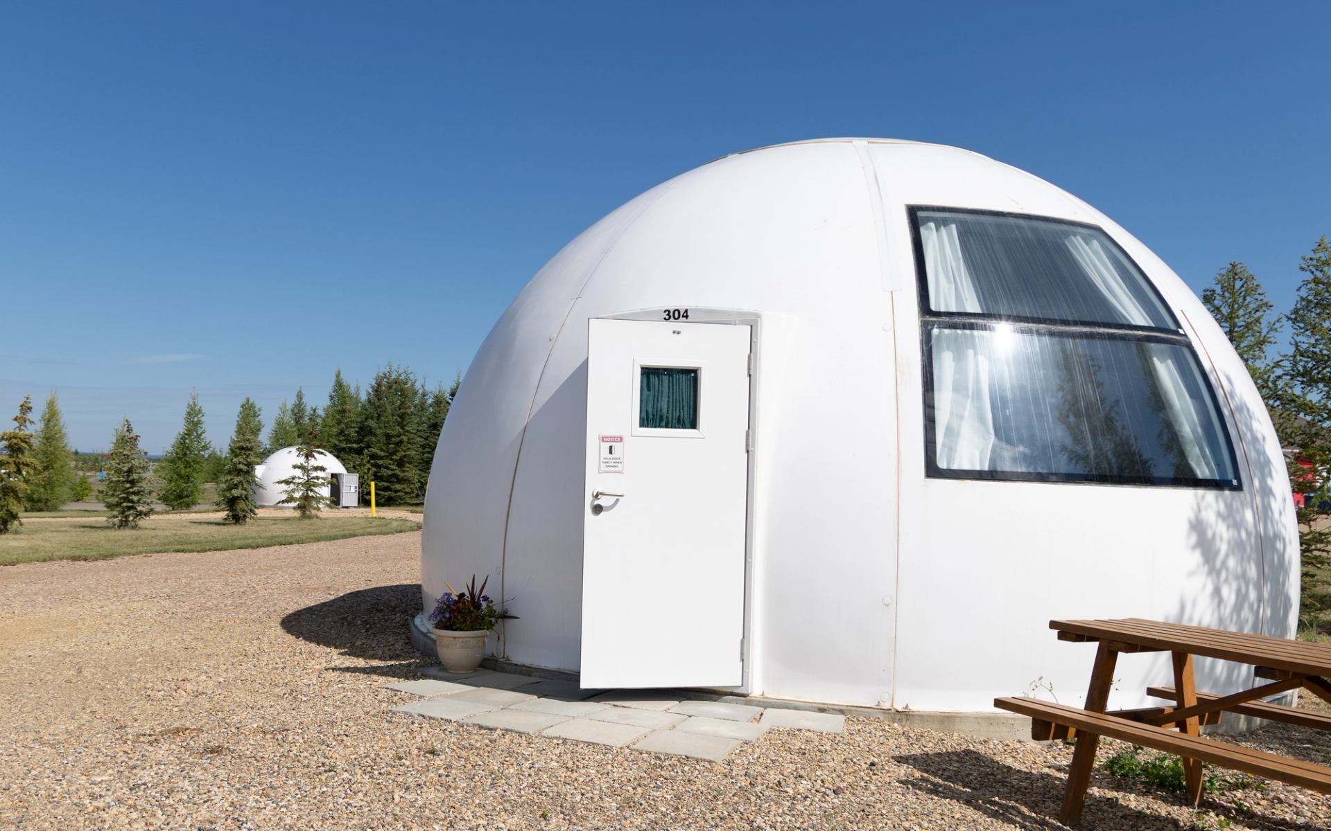 White dome cabin with open door, large window and picnic table.