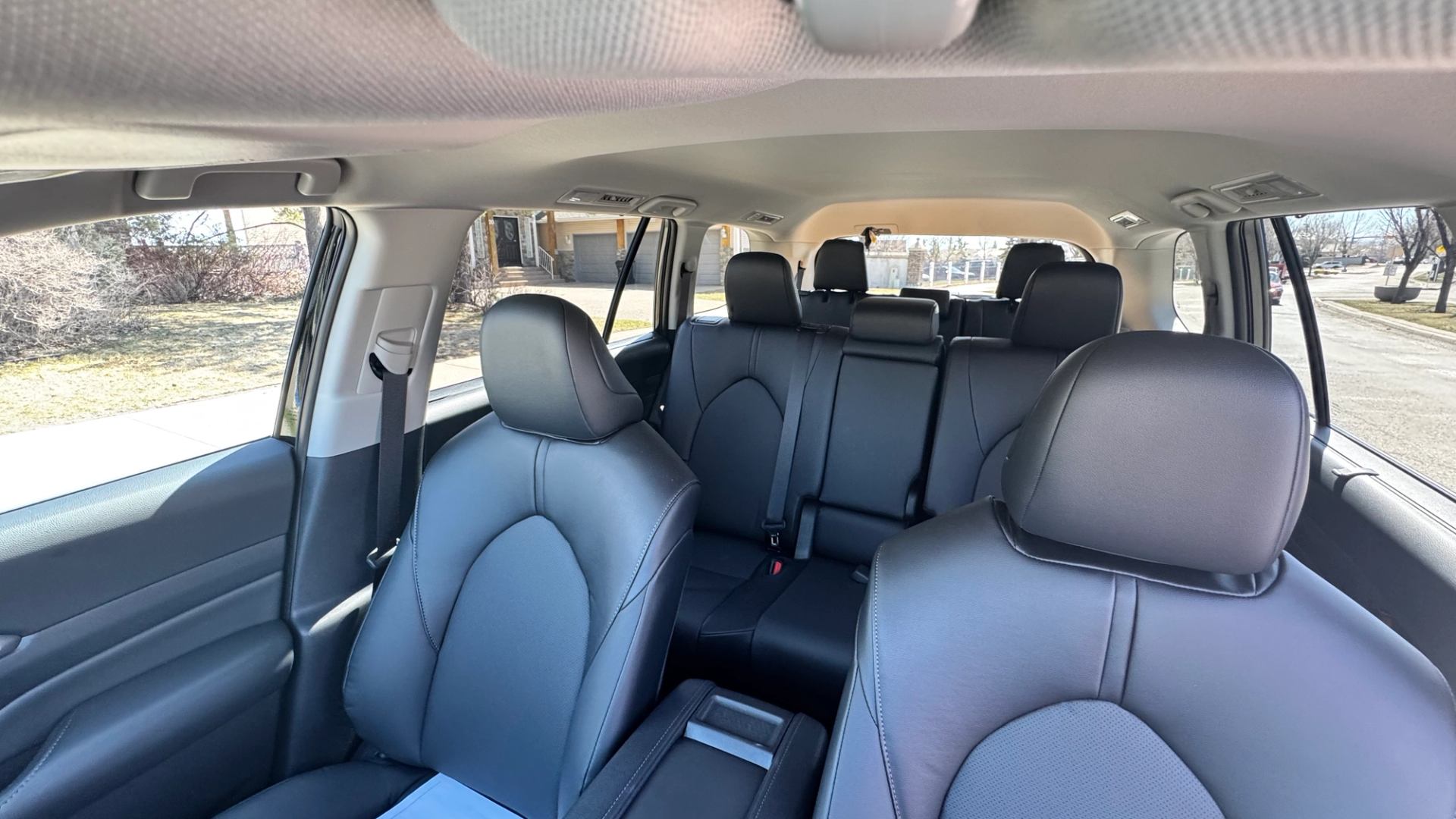 Wide view of SUV interior with three rows of black leather seats and windows.