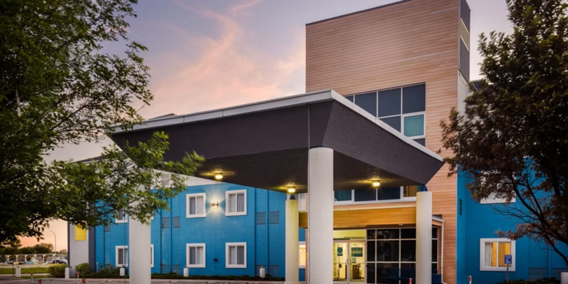 Blue and wood-clad building entrance with a large illuminated canopy and white columns.