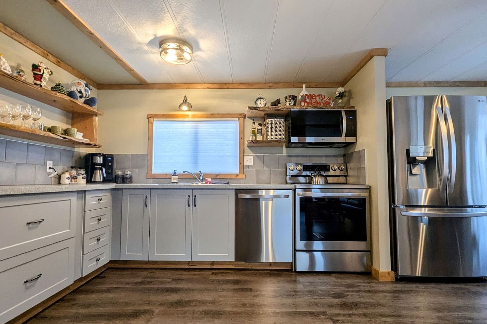 A kitchen with light grey cabinets, stainless steel appliances, and wooden open shelves.