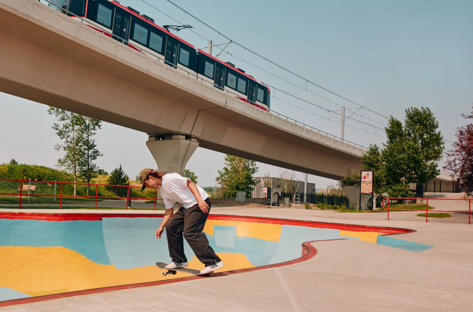 A young man skateboards at the Millenium skatepark underneath an elevated C-Train line.