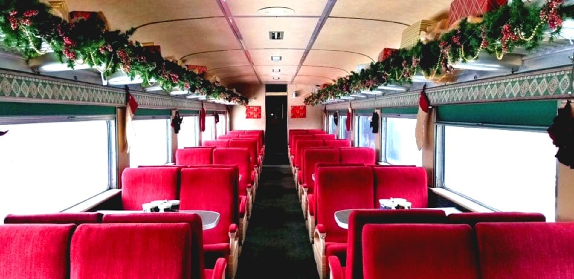 Train carriage with red seats, large windows and festive garlands along overhead racks.