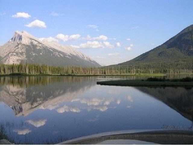 Mountain lake with clear reflections and scattered clouds in a peaceful landscape.