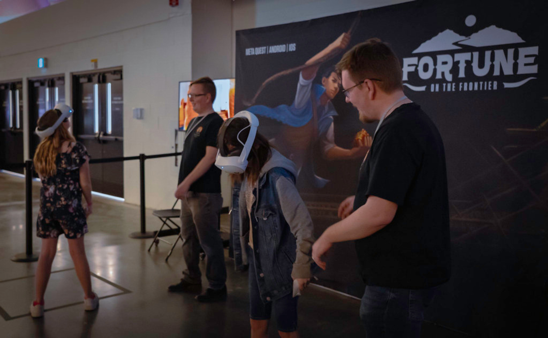 People using VR headsets at an event booth with a large display backdrop.