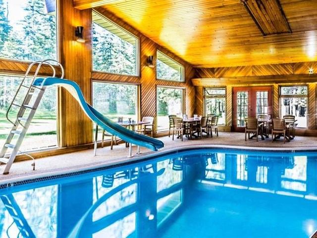 Indoor pool with wooden walls and dining chairs near large windows.