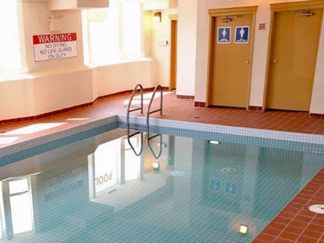 An indoor swimming pool with blue tiles, a metal ladder, and a warning sign on the wall.