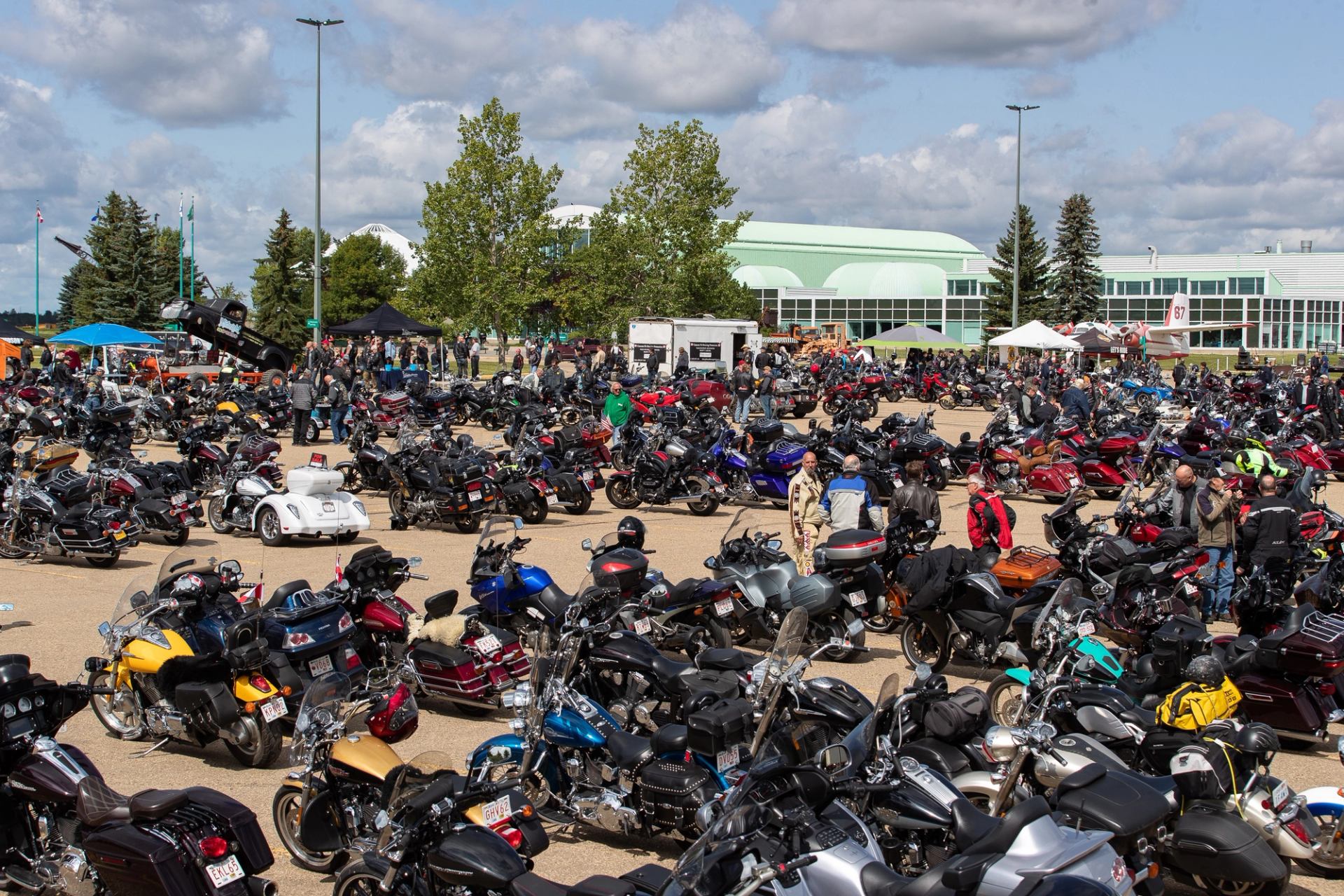 Motorcycle parking lot with rows of bikes outside large green-and-white building.