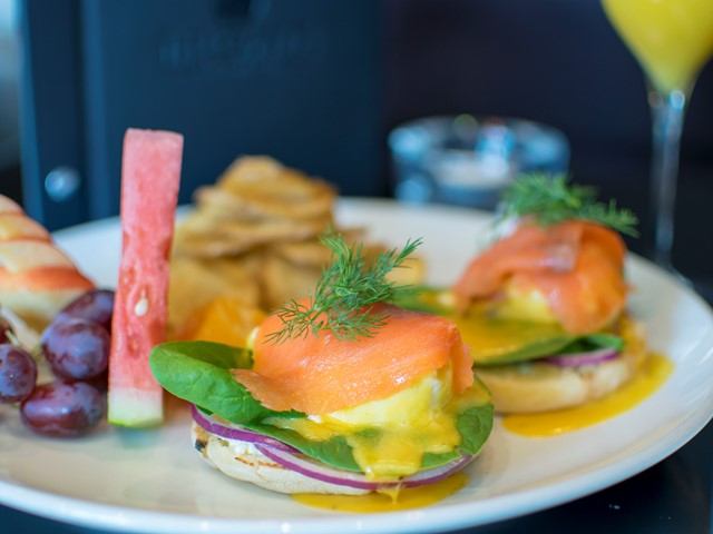 Eggs benedict with smoked salmon, fruit, and chips on a white plate.