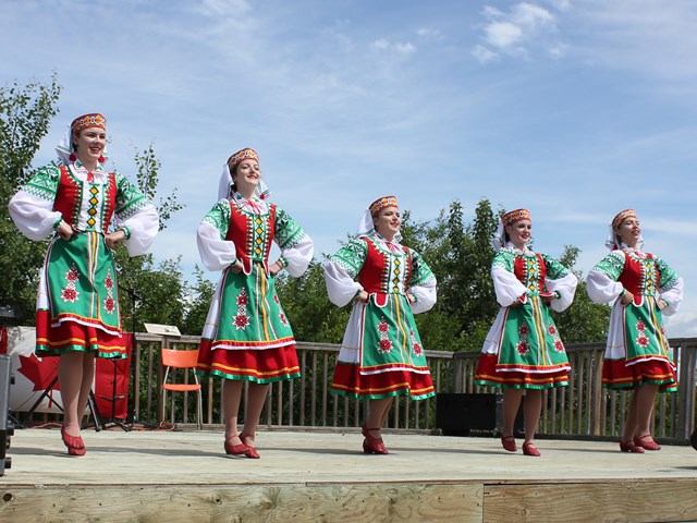 Folk dancers in green and red embroidered costumes perform on outdoor stage at historic site.
