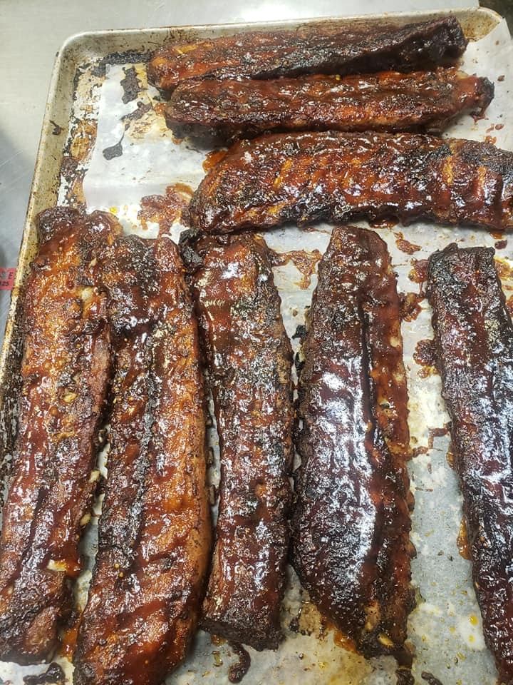Platter of grilled pork ribs with charred edges and barbecue sauce drips.