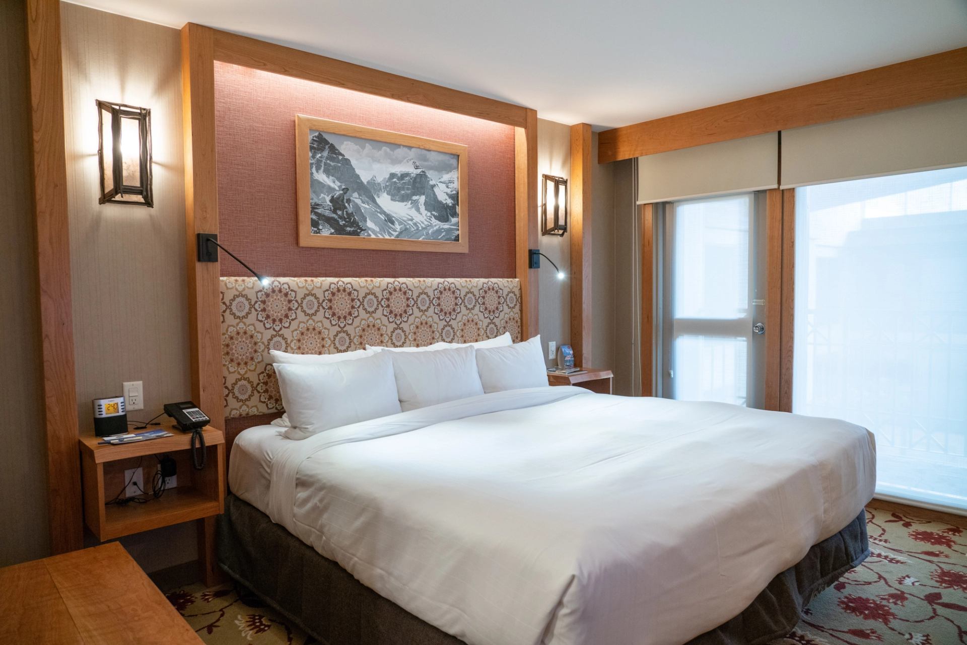 Cozy hotel room with mountain art, white linens, and warm lighting.