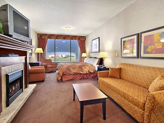Hotel suite with a cozy seating area, fireplace, coffee table, and bed near a large window.