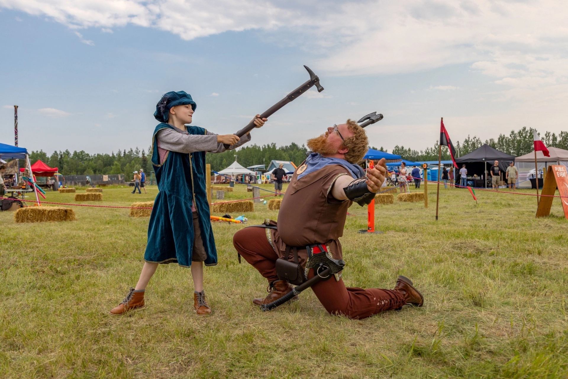 Performer raises weapon over kneeling figure at outdoor Renaissance fair.