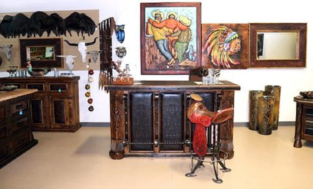 Art gallery display with painted pictures, wooden cabinet, and metal artwork on showroom walls.