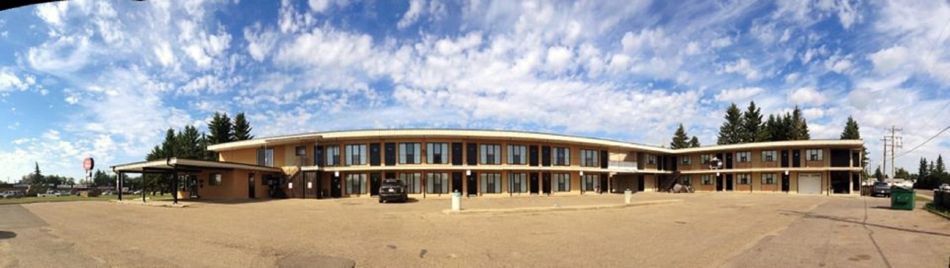 Two-story motel with balcony, large windows, and parked cars under a partly cloudy sky.