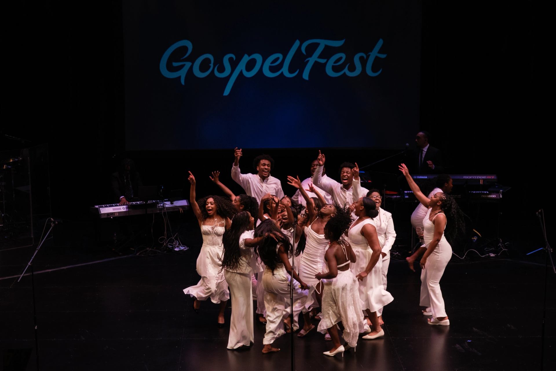 Gospel choir in white outfits performs energetically onstage under large GospelFest sign.