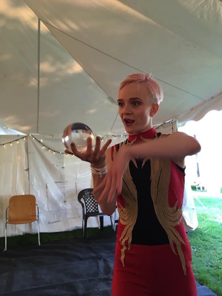 Performer in red costume manipulates clear acrylic ball under a large event tent.