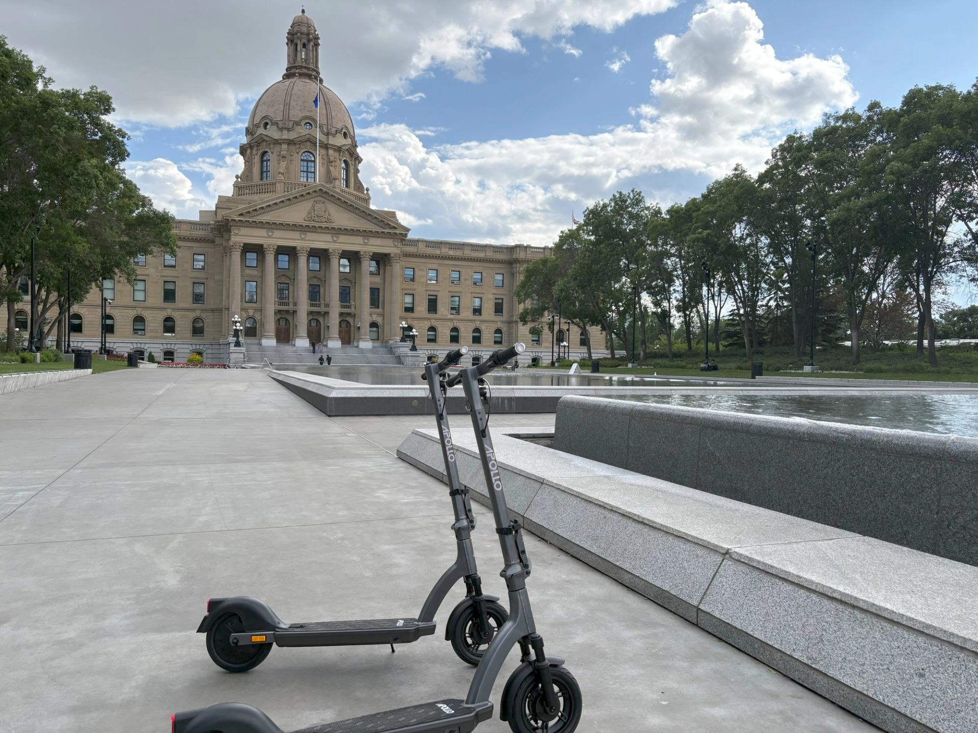 Two electric scooters parked near a domed historic building with fountains and trees.