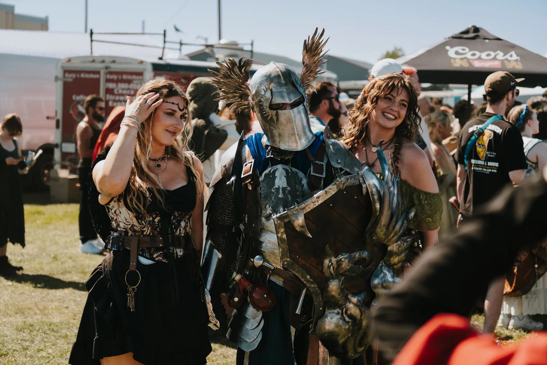 Group in medieval and fantasy costumes at outdoor faire with tents and trailer in background.