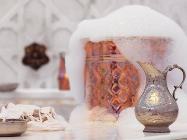 Copper container with soap suds and ornate pitcher in a vintage-style washing area.