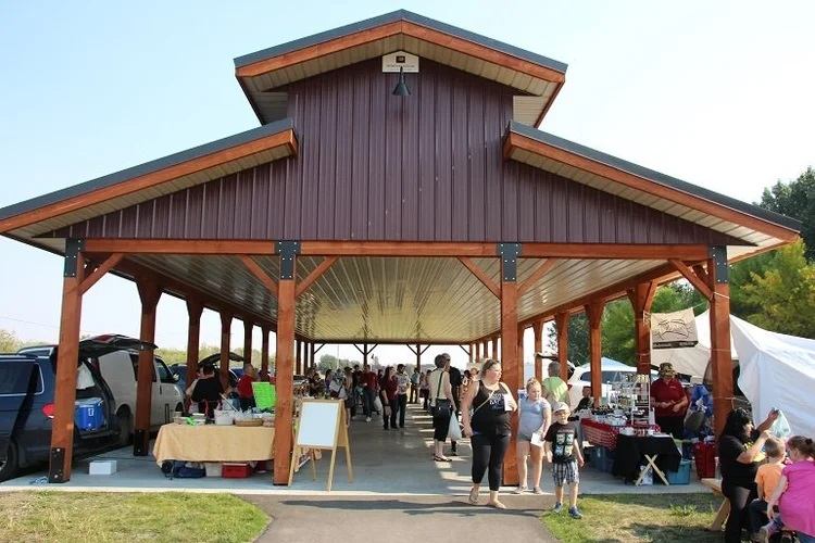 Visitors explore vendor booths beneath a covered market pavilion with tables and displays throughout.