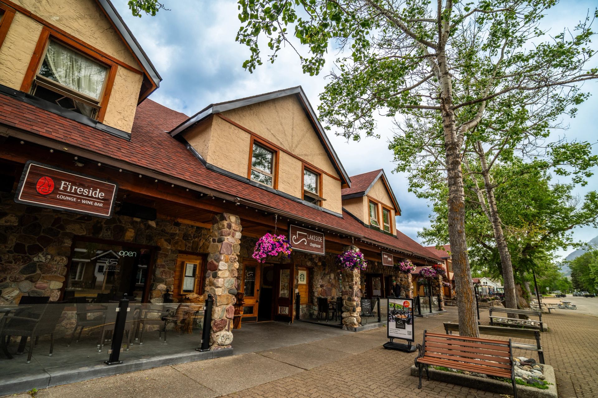 Stone-front shops with Fireside Lounge sign, hanging flower baskets and benches along sidewalk.