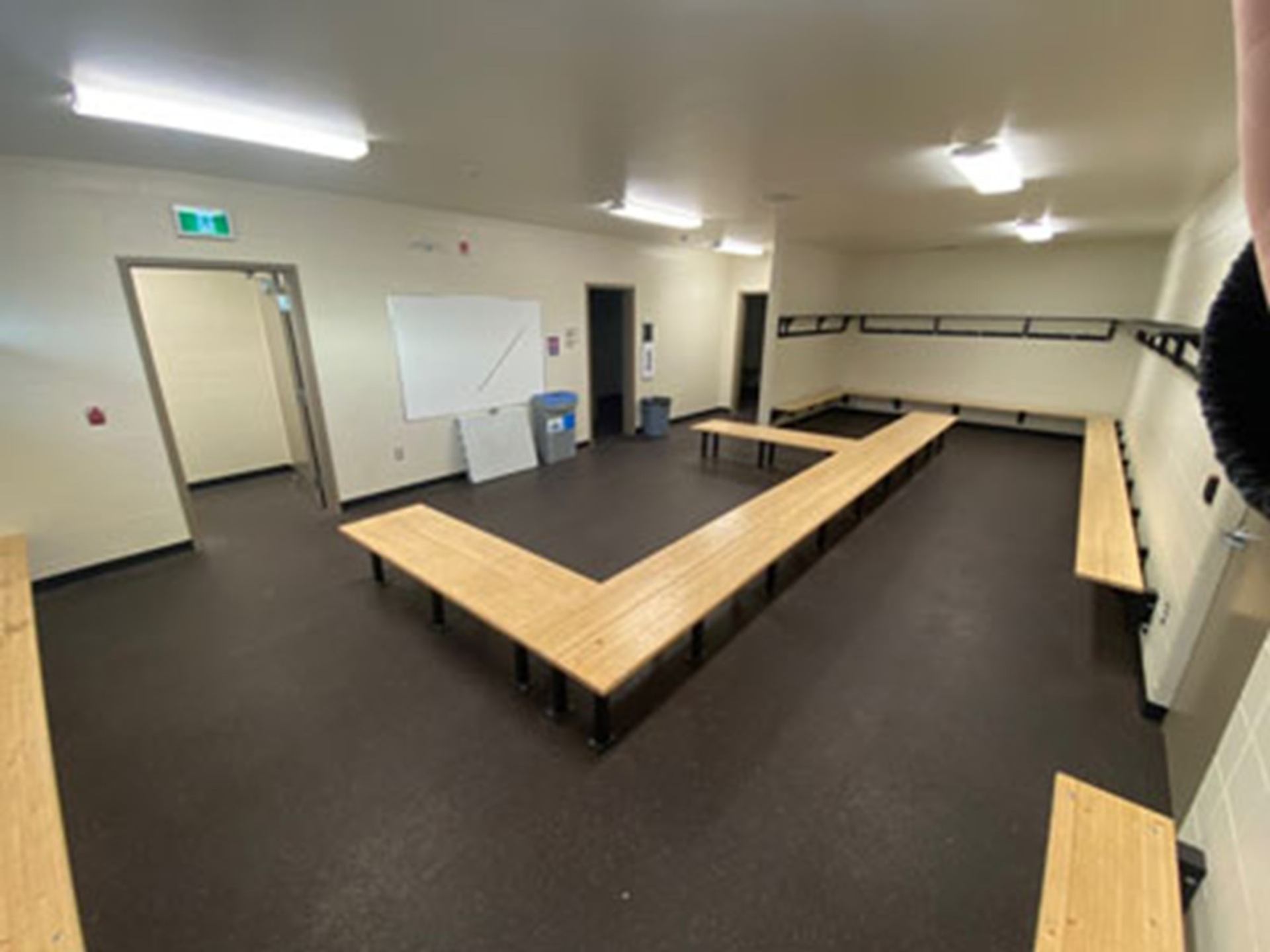 Empty locker room with wooden benches, wall hooks, whiteboard and recycling bin.