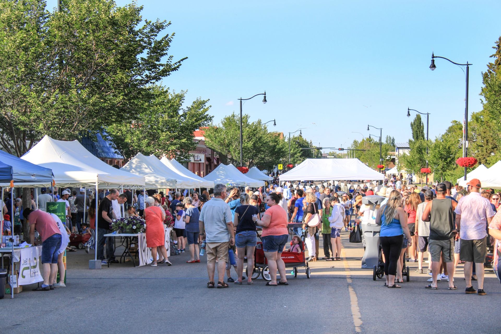 Busy outdoor market with people and white vendor tents lining a street.