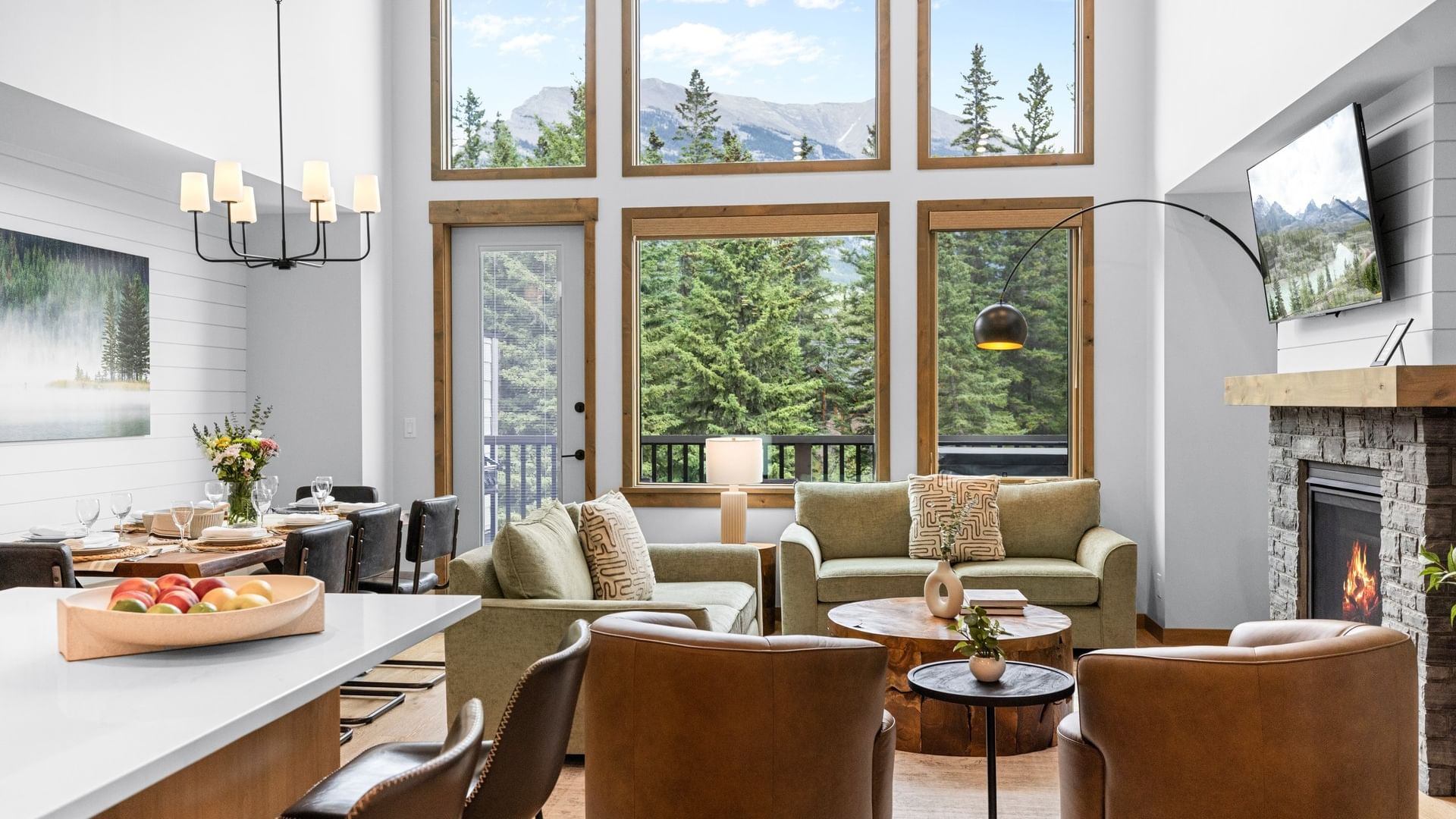 Open-concept living room with fireplace, dining area and mountain views through large windows.