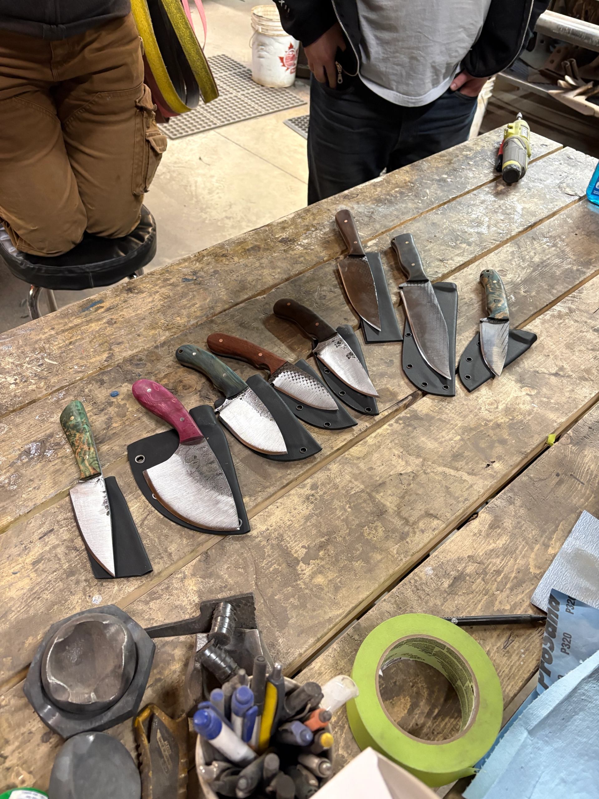 Handmade knives with sheaths displayed on a workshop table.