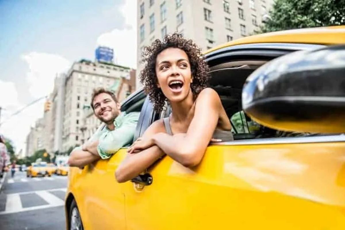 Two people lean from a yellow taxi's windows on a city street.