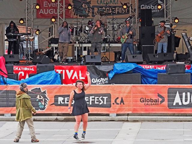 Outdoor stage at reggae festival with musicians and banners reading “Reggae Fest, Calgary”.